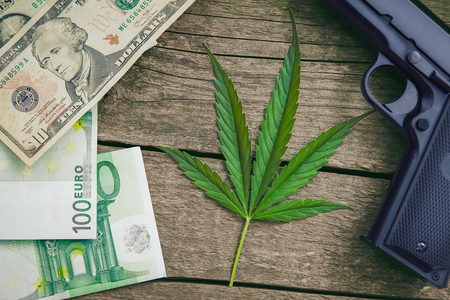 Cannabis leaf.Gun and money around leaf on wooden background.の写真素材