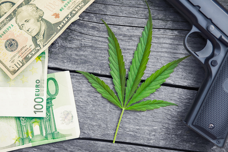Marihuana leaf.Gun and money around leaf on wooden background.の写真素材