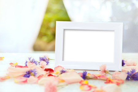 White picture frame on wooden table with petals and flowersの写真素材