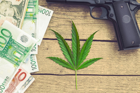 Marihuana leaf on wooden background with gun and money billsの写真素材
