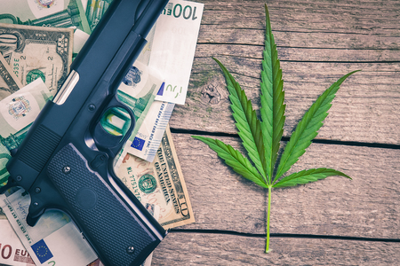 Marihuana leaf with banknotes and weapon on the tableの写真素材