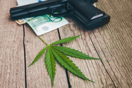 Cannabis leaf with gun and money bills on wooden tableの写真素材