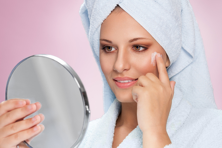 Close-up young beautiful face of girl applying moisturize cream and holding mirrorの写真素材