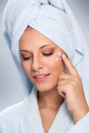 Young woman applying cosmetic cream on a clean fresh face, skincare concept.の写真素材