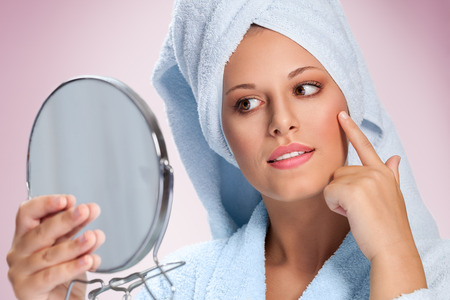 Beautiful spa woman looking her skin in mirror. Skincare concept.の写真素材