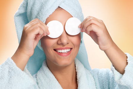 Woman in bathrobe holding cotton pads on her eyesの写真素材