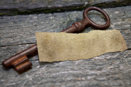 Rusty vintage key with white piece of paper on old tableの写真素材