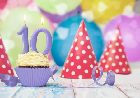 Single muffin for tenth birthday with party hats and blue ribbon on the tableの写真素材