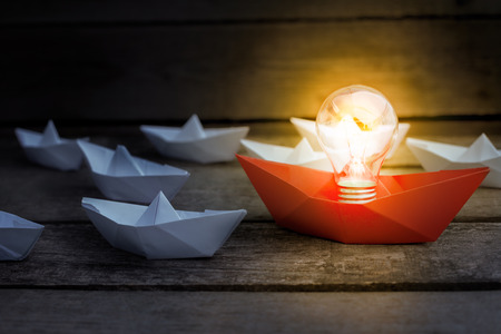 Team leader importance presented with glowing bulb and paper boats in team of workers の写真素材