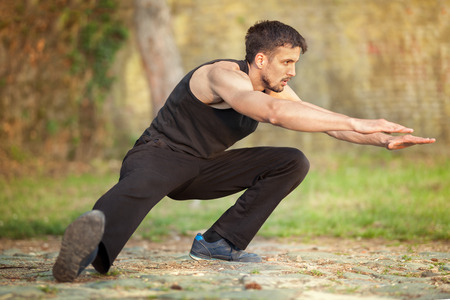 Young muscular man runner stretching legs before running, workout in natureの写真素材