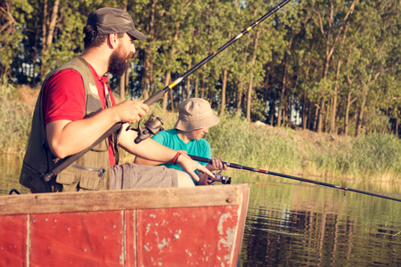Dad and son fishing at lake in the countryside, they sitting with fishing rods and waiting for catchの写真素材