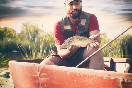 proud attractive fisherman showing fish, smiling man fishing as weekend hobbyの写真素材