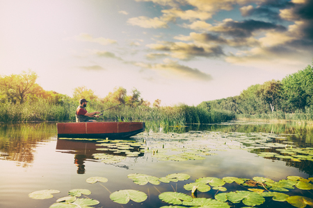 Fisherman in wooden boat with fishing rod catching fishの写真素材