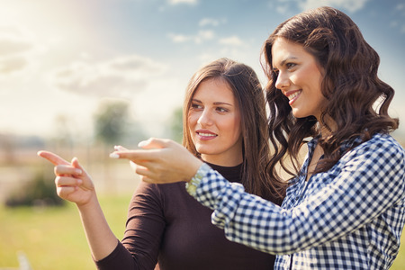 Two young pretty women in a park their points at something の写真素材