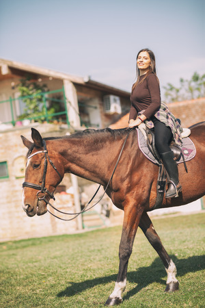 attractive brunette female rider sitting on her horse and smilingの写真素材