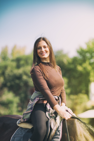 Young beautiful brunette girl rides a horse on a warm and sunny day. Portrait of a pretty young woman on the horseの写真素材