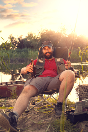 Man fishing and enjoy in drink and  last rays of sunlight on lake shoreの写真素材