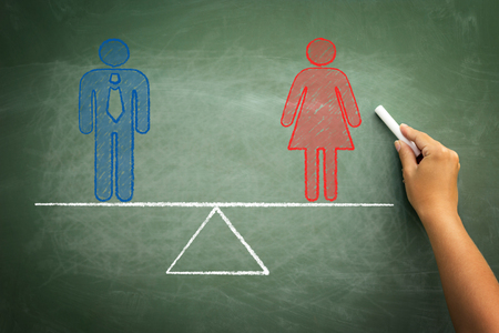 Man equal to woman gender equality concept on green chalkboard with hand holding chalkの写真素材