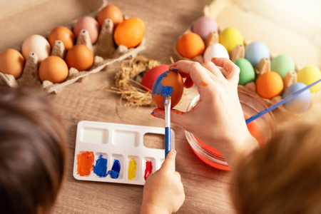Little girl painting Easter eggs at the table. The girl is 3. The kids are having fun in sunny room.の写真素材