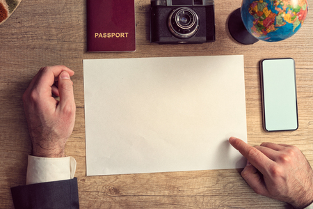 Businessman planning a trip around the world, he is pointing on empty paper and using a mobile app, vacations and holidays conceptの写真素材