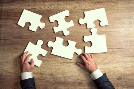 Close-up of businessman hands try to completing jigsaw puzzle, solving a business problemの写真素材