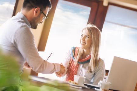 Smiling businesspeople shaking hands together while standing at cafeの写真素材