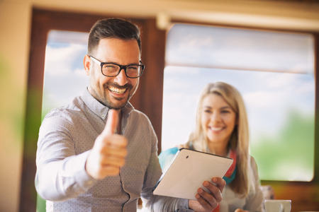 Smiling businessman with tablet pc computer showing thumbs up with happy businesswoman in back, success teamwork and  business conceptの写真素材