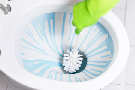 Woman in green  rubber gloves is cleaning toilet bowl using detergentの写真素材