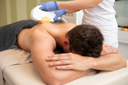Young man receiving laser treatment epilation, remove hair from his backの写真素材