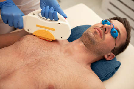 Close-up of beautician giving laser epilation treatment to young man chestの写真素材
