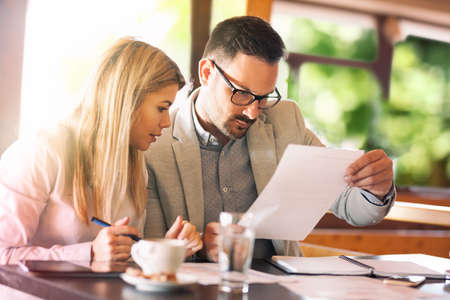Businessman explaining something to female colleague on project document at desk in cafeの写真素材
