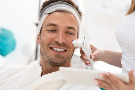Smiling man looking at tablet type and condition of the his skin measured by the skin scannerの写真素材