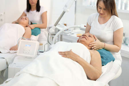Mother and daughter had a day of spa. They are in white bath towels and lying on cosmetic deskの写真素材