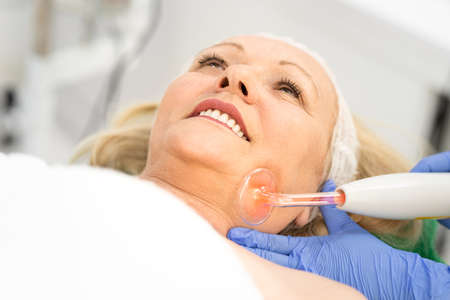 Beautiful senior, gray hair, woman getting a facial treatment. Concept of skincare, cosmetics, beauty salon, facial treatment, facial massage, wellbeingの写真素材