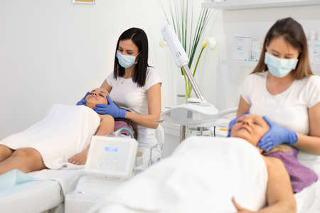 Mother and adult daughter enjoy beauty treatment in a spa center. Beauty treatment. Beauticians applying facial mask on young adult and senior women's face.の写真素材