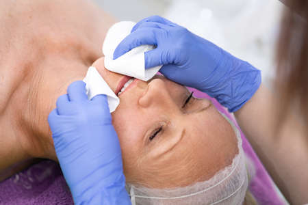 Skin care. Senior woman cleaning face by beautician with cotton padの写真素材