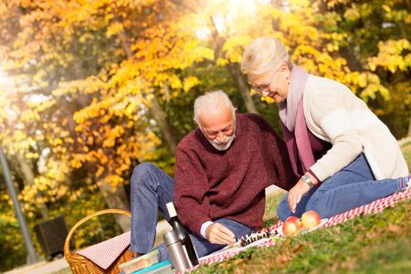 Senior couple with picnic playing chess in autumn parkの写真素材
