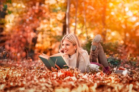 Beautiful girl with book in the autumn park lying in grassの写真素材