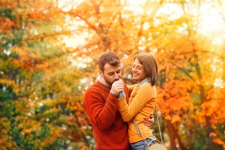 Couple in love on sunny autumn day  rays in the park. Young man kissing hand his adorable girl in...