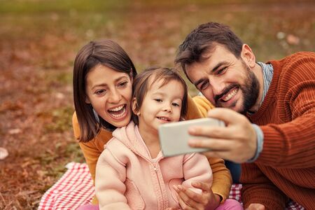 Happy family taking selfie while sitting on picnic blanket at beach during sunny day