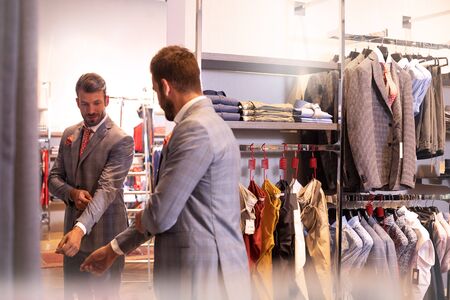 Young handsome man trying suit on mirror in menswear shop