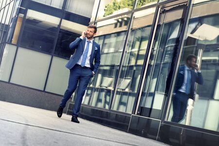 Full length portrait of a confident young businessman walking in the city talking on cell phoneの写真素材