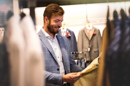 Handsome man in in menâs cloths store, holds his pants in his hands and looks at them with a smile "I was just looking for this"の写真素材