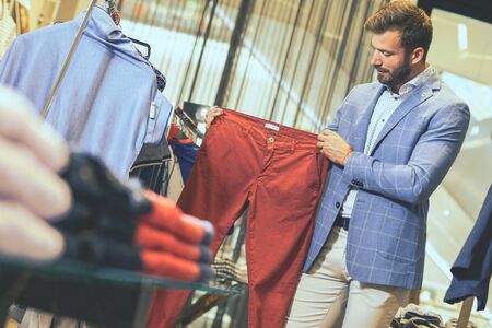 Man in clothing store choosing pantaloons so he is looking for color that will match his style.の写真素材