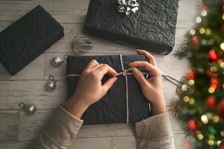 Young woman wrapping Christmas gifts on wooden table