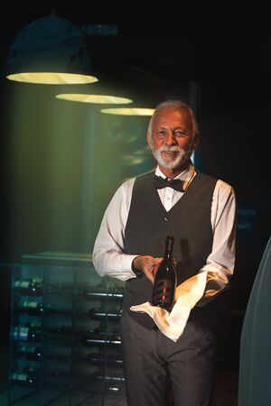 Positive sommelier displaying a bottle of wine in modern winery cellarの写真素材