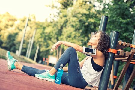 Sporty young woman with smart phone on her arm and is listening to music. Relaxing. Copy space. She...
