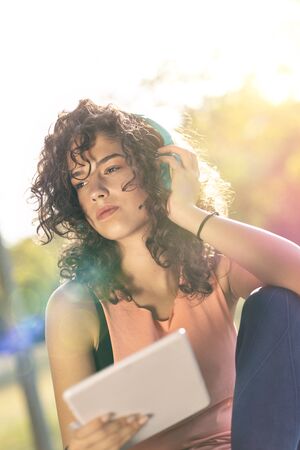 Young woman relaxing at park after training using a tablet computer and headset,  looking very happy