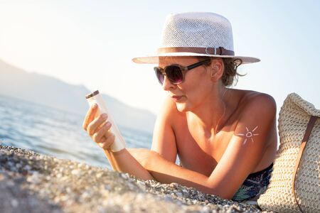 Woman hands putting sunscreen from a suntan cream bottle. Caucasian female squeeze suncream on her...