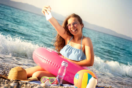 Smiling young girl with big tires for swimming taking selfie in summer on beach